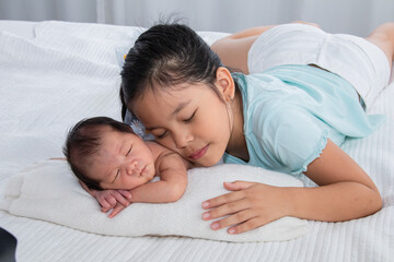 Cute Asian big sister and newborn baby sleep on bed, Girl and adorable infant lying on white bed at home. sister and brother spend time together. Toddler deeply sleeping with safe and relax.