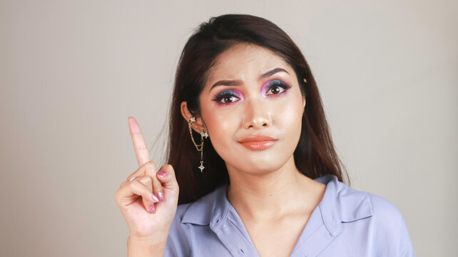 Portrait of beautiful young Asian woman confuse and pointing fingers upward at copy space isolated over white background