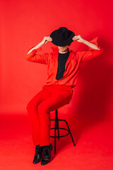 Tall handsome man dressed in red shirt, trousers and black hat posing on the red background