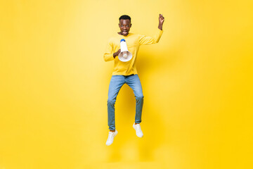 Fototapeta na wymiar Jumping portrait of young African man yelling on megaphone in isolated yellow color background