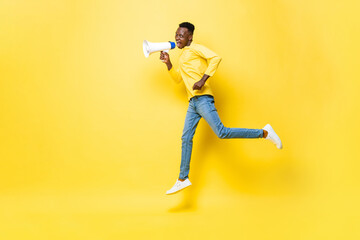 Fototapeta na wymiar Jumping portrait of young African man holding megaphone and shouting in isolated yellow color studio background