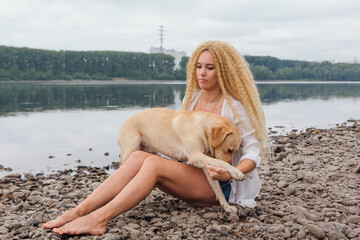 Young woman sitting with her labrador retriever dog on the river shore