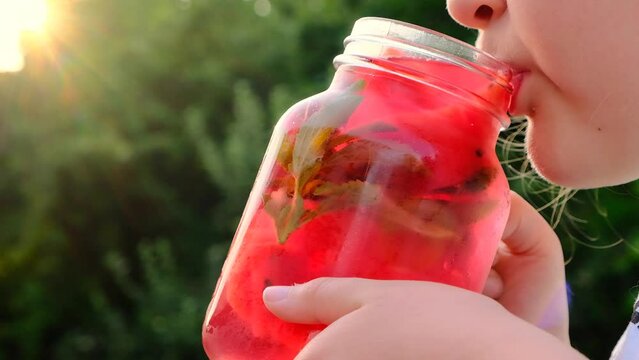 watermelon drink with stevia.little girl drinks a watermelon drink from a mug in a summer garden. child drinks a red cold cocktail from a glass misted mug.Watermelon diet smoothie. High quality 4k