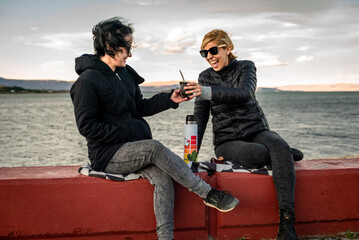 Caucasian and Hispanic females sitting against the seascape and drinking yerba mate in Argentina