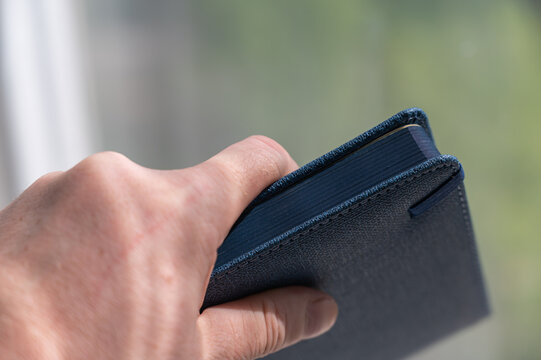 A man's hand holds a closed diary. Blue hardcover notebook. Close-up. Selective focus.