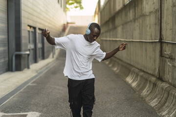 Young cool black male in a street style outfit dancing with blue headphones outdoors