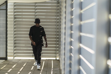 Young cool black male in a street style outfit posing in a room with blinds