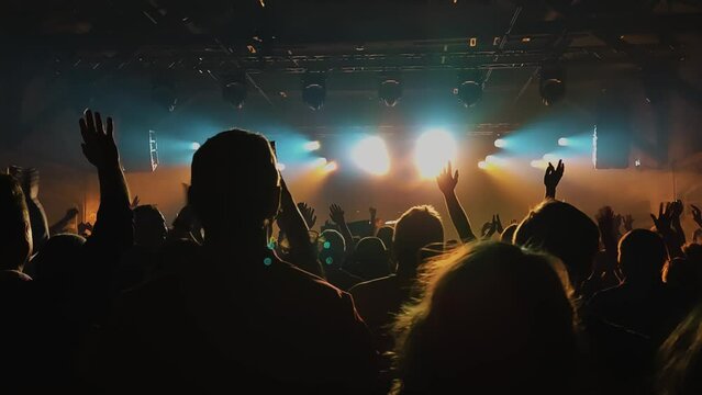 Unrecognizable Fans Dancing and Raising Their Hands at a Concert or Festival Party. Silhouettes of Crowd Audience Enjoying Concert  in Front of Bright Stage Lights.