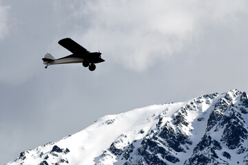 Fototapeta na wymiar A single-engine airplane flies over snow-covered Alaska mountains