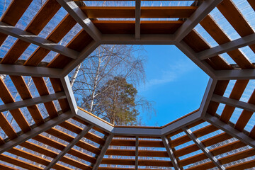 View of blue sky through wooden frame, lattice. Window on roof of alcove, view of sky and treetops. Calm and serenity on clear spring day