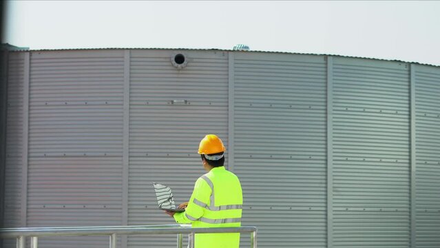 Engineer using laptop examine the construction of water tanks  steel metal sheet for tap water water storage of industrial estate. Utilities of industry.