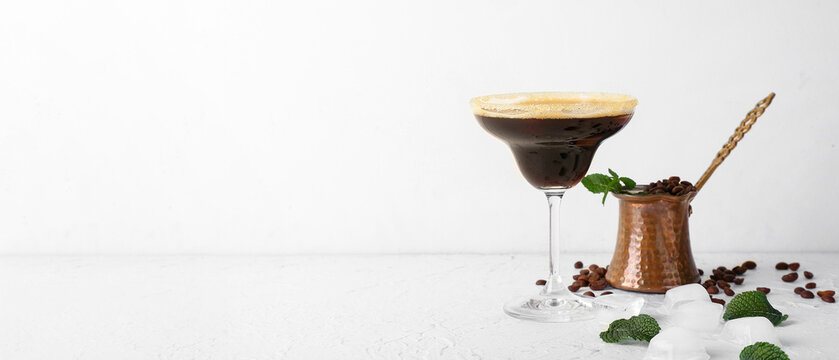 Glass of tasty espresso martini cocktail and jezve on light background with space for text