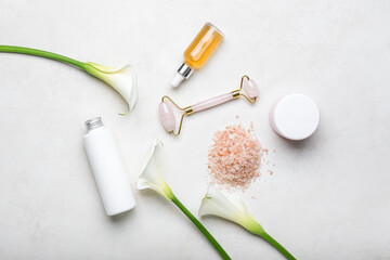 Composition with cosmetic products, sea salt, facial massage tool and calla lilies on light background