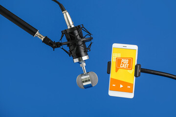 Microphone and mobile phone with word PODCAST on screen on blue background, closeup