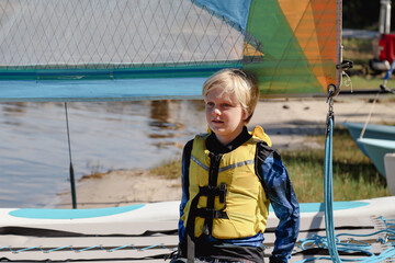Young boy wearing yellow life jacket sitting on boat ready to go sailing