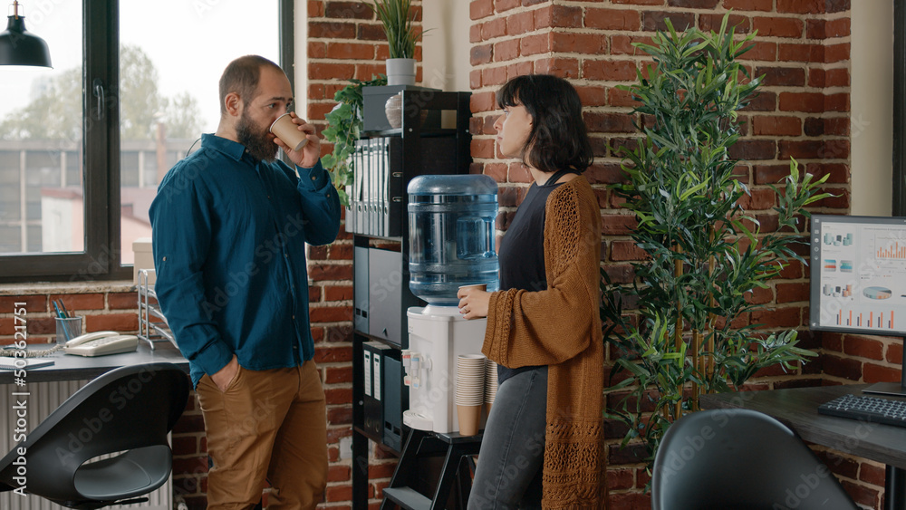 Wall mural colleagues on break having discussion and using water cooler in business office. man and woman talki