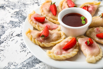 Plate with delicious strawberry dumplings and jam on grunge background, closeup