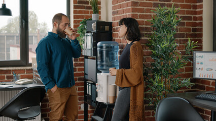 Colleagues on break having discussion and using water cooler in business office. Man and woman...
