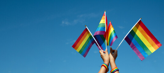 Rainbow flags showing in hands against clear bluesky, copy space, concept for calling all people to support and respcet the genger diversity, human rights and to celebrate lgbtq+ in pride month. - obrazy, fototapety, plakaty