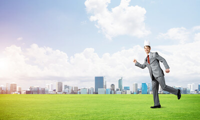 Fototapeta na wymiar King businessman in elegant suit running on green grass and modern cityscape at background