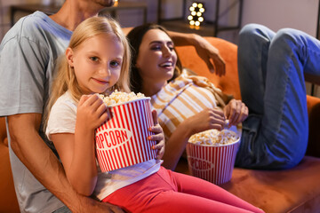 Young family with popcorn watching movie at home in evening
