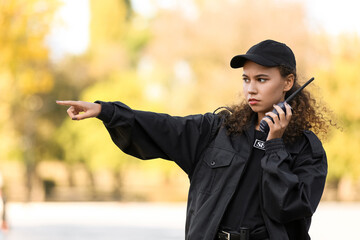 African-American female security guard with radio transmitter pointing at something outdoors