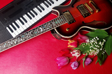 Fototapeta na wymiar Electric guitar, synthesizer keyboard and a bouquet of tulips on a red table.