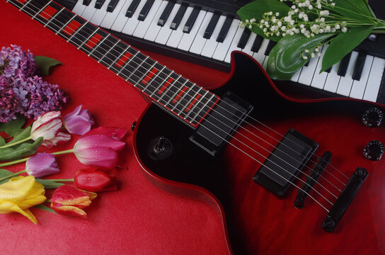 Electric guitar, synthesizer keyboard and a bouquet of tulips and lilies of the valley on a red table.