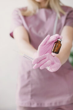 A woman in a pink surgical suit and medical gloves holds a syringe and an ampoule. Hands in latex gloves close-up. Treatment and health care. Beauty injections and beauty treatments