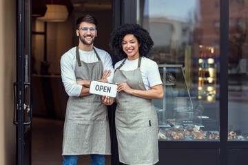 Two owners friends holding a open poster together while smiling to the camera in front of pastry...