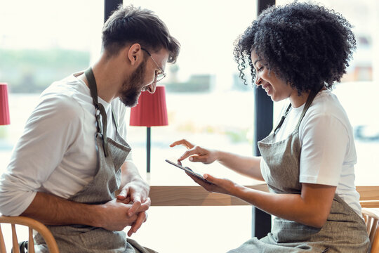 Couple owners bakery working while analyzing report for order delivery with digital tablet in a pastry shop.