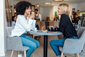 Young happy women talking and laughing while drinking coffee together in pastry shop.