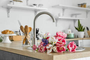 Bouquet of flowers in sink on counter with kitchen utensils
