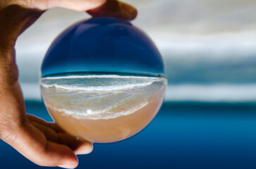 A beautiful Ocean beach view photography in clear crystal glass ball with left male hand holding.