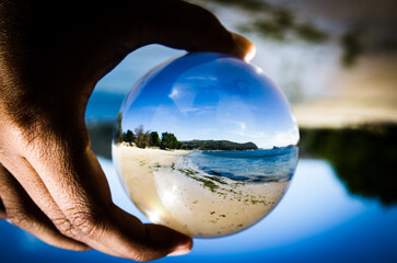 A beautiful Ocean beach view photography in clear crystal glass ball with left male hand holding.