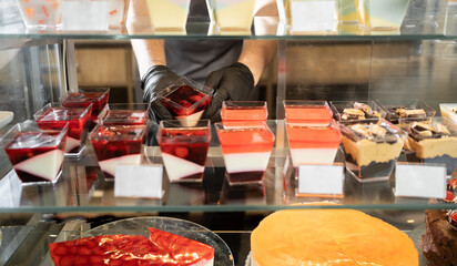 showcase with sweets jelly desserts in the refrigerator behind glass. popular food business in the city concept male hand takes one.