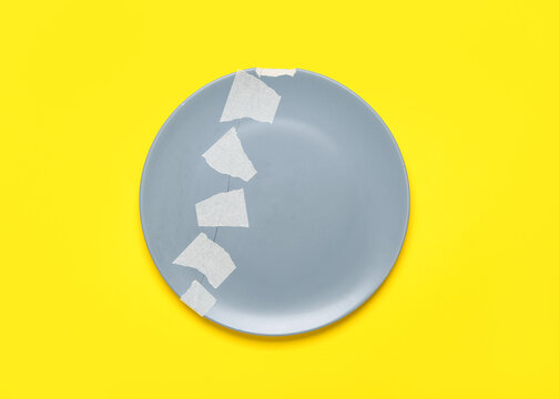 Broken ceramic plate with adhesive tape on yellow background