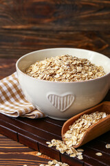 Bowl and scoop with raw oatmeal on wooden table, closeup