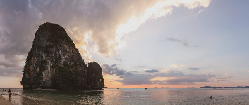 Mesmerizing view of a cliff in the water near a sandy beach and a person walking at scenic sunset