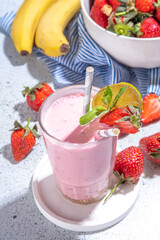 One glass with Strawberry banana milkshake, with fresh fruits on white concrete table, copy space