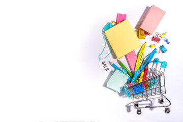 School sale concept. Shopping supermarket cart with colorful paper bags, school education supplies and accessories. Back to school shopping background, copy space