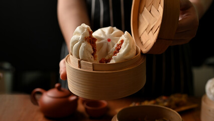 Female chef holding a bamboo steamer with tasty original Chinese steamed pork buns.