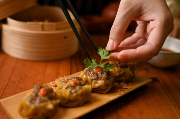 Female chef using chopsticks, garnishing steamed pork or meat dumplings with coriander leaf.