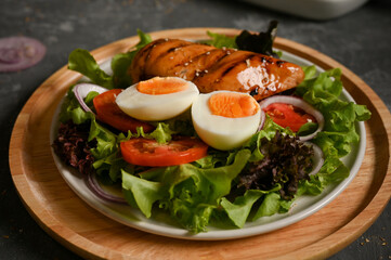 Chicken breast steak salad served with boiled egg on a kitchen table.