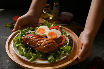 Female hands holding a plate of roasted chicken breast with fresh organic salad