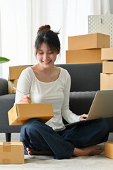 Beautiful female business entrepreneur writing a customer's address on a parcel box.