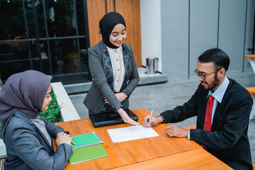 portrait of businessman signing an agreement letter during meeting with female muslim partner