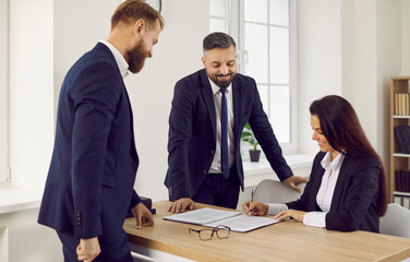 Successful deal. Business people at meeting in office sign contract confirming partnership agreement. Three professional, confident and stylish business partners find compromise sign important deal