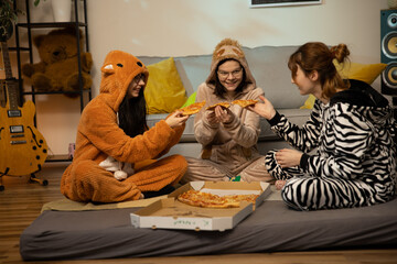 Happy female friends having good time at pajama party in the bedroom. friendship, people, pajama party, entertainment and junk food concept