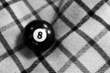 Grayscale shot of a billiard ball number 8 on a checkered fabric